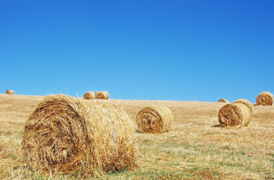 View of hay bales on field against clear blue sky