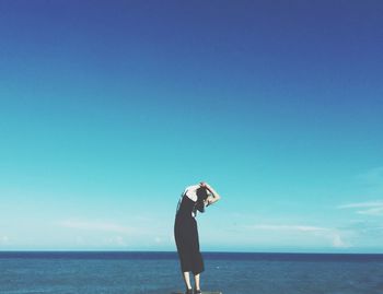 Full length of woman standing on sea against blue sky