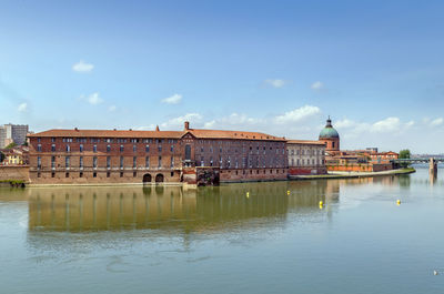 Buildings at waterfront against cloudy sky