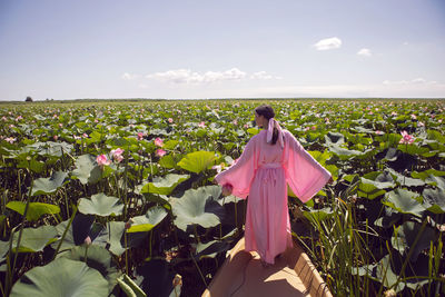 Portrait brunette woman  in a pink dress stands on a boat in the river among the lotuses in summer