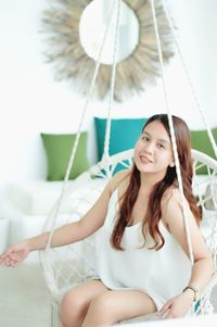 Portrait of smiling woman sitting on hanging chair at home