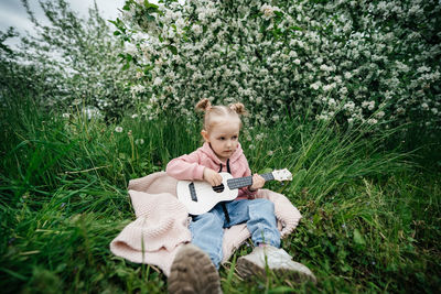 Little girl playing the ukulele in a blooming apple orchard in nature