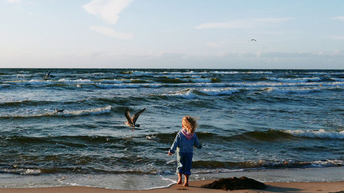 Rear view of little girl standing at beach against sky. flying seagull