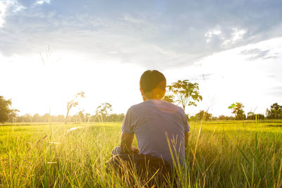 Rear view of man sitting on field against sky