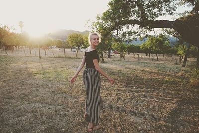 Portrait of young woman standing on field against sky