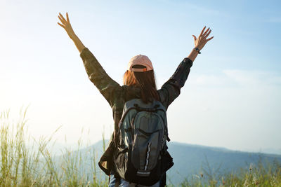 Rear view of hiker standing with arms raised against mountains