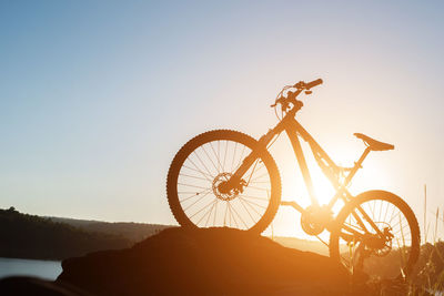 Silhouette bicycle on rock against clear sky during sunset