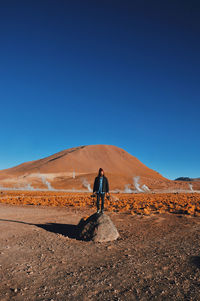 Full length of man standing on desert against clear blue sky