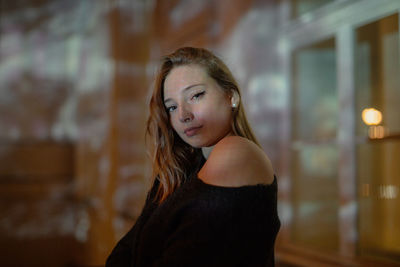 Portrait of young woman standing against building at night