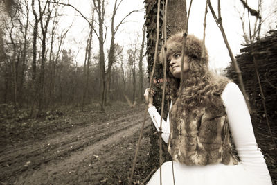 Thoughtful woman in jacket by tree at forest