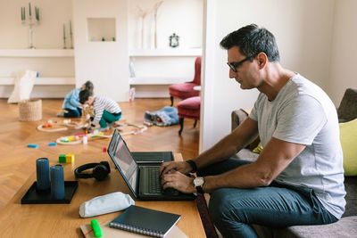 Father typing over laptop while children playing in background at home