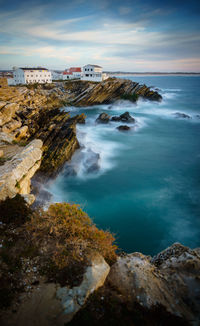 Houses on rock formation in sea at baleal island against sky