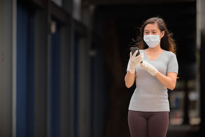 Woman wearing mask and gloves while using phone outdoors