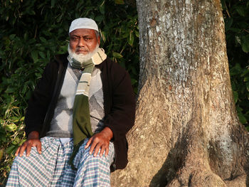 Portrait of old man sitting on the tree trunk