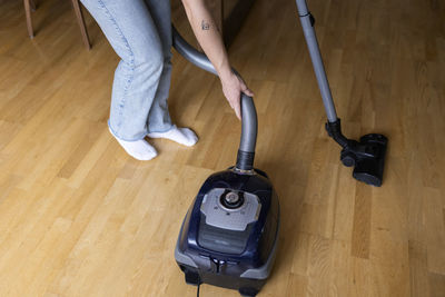 Low section of young woman using vacuum cleaner on hardwood floor at home