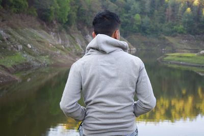Rear view of young man looking at lake while sitting in forest