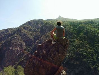 Rear view of man climbing on mountain against sky