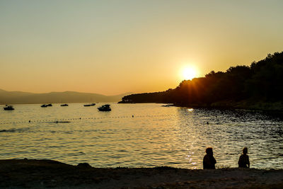 Silhouette people on beach against sky during sunset