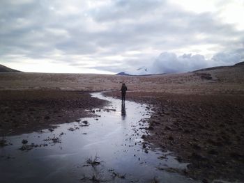 Woman standing in stream on mountain against cloudy sky