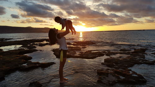 Mother and baby against sky at sunset