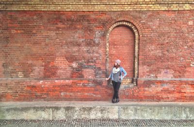 Full length of young woman standing against brick wall