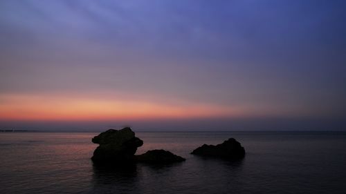 Rock formation in sea against sky during sunset