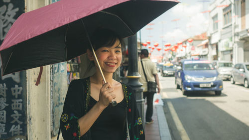 Woman holding umbrella while standing on sidewalk in city