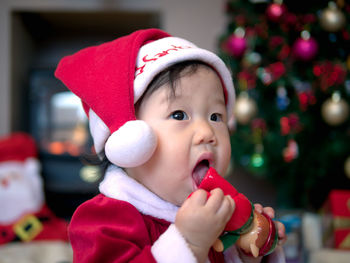 Cute baby girl wearing santa hat against christmas tree at home