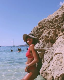 Woman on rock by sea against clear sky