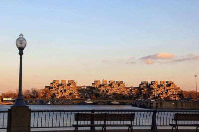 Promenade by lake in city against sky during sunset