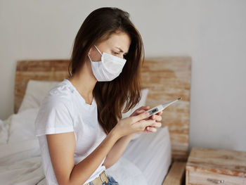 Young woman using mobile phone while sitting on bed