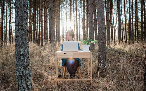 Woman travelling working on a desk and laptop in a forest at sunset