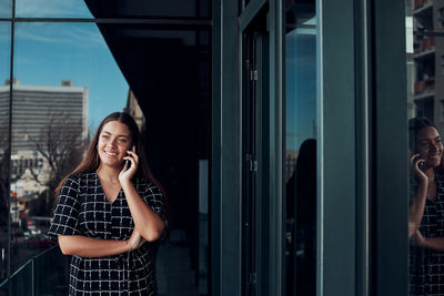 Full length of smiling woman standing on mobile phone