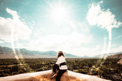 Woman sitting on mountain against sky on sunny day