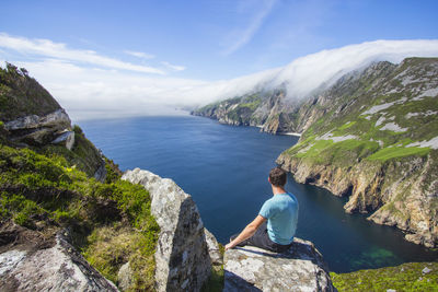 Man looking at view while sitting on rock formation by sea against sky