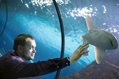 Young man touching fish in aquarium