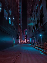 Empty road amidst illuminated buildings in city at night