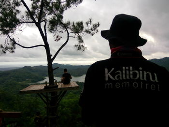 Rear view of men sitting on mountain against sky