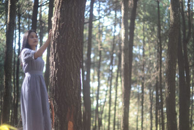 Woman standing by tree trunk in forest