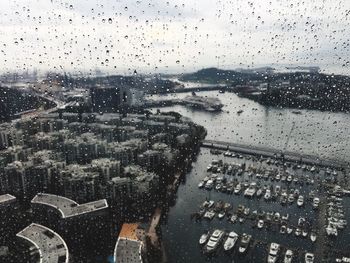 Boats moored at harbor by city seen through window during rainy season