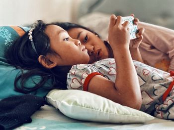 Girl using phone while lying on bed by sister at home