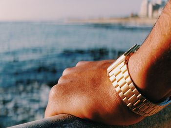 Cropped hand wearing wristwatch by river on sunny day