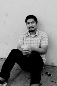 Portrait of smiling young man sitting against wall