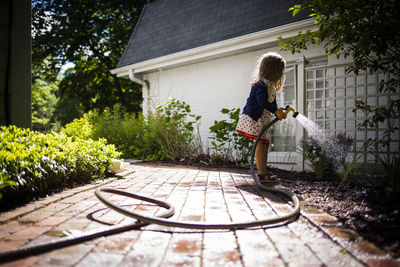 Side view of girl watering plants in backyard