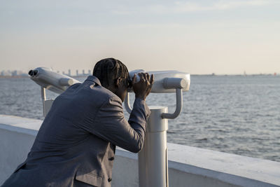 Businessman looking through coin-operated binoculars at sunset