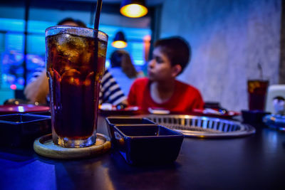 Close-up of cold drink served on table with boy in background at restaurant