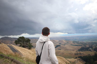 Rear view of man looking at landscape against cloudy sky