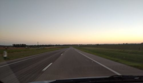 Road passing through field against sky during sunset