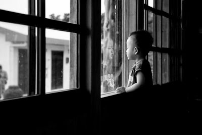 Side view of boy looking through window at home