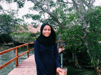 Portrait of smiling young woman standing against trees